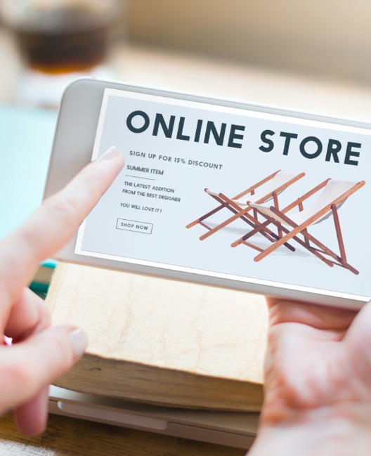 A person browses an online store on a smartphone, viewing a page featuring wooden deck chairs. The text on the screen mentions a 15% discount and encourages signing up to enjoy the offer.